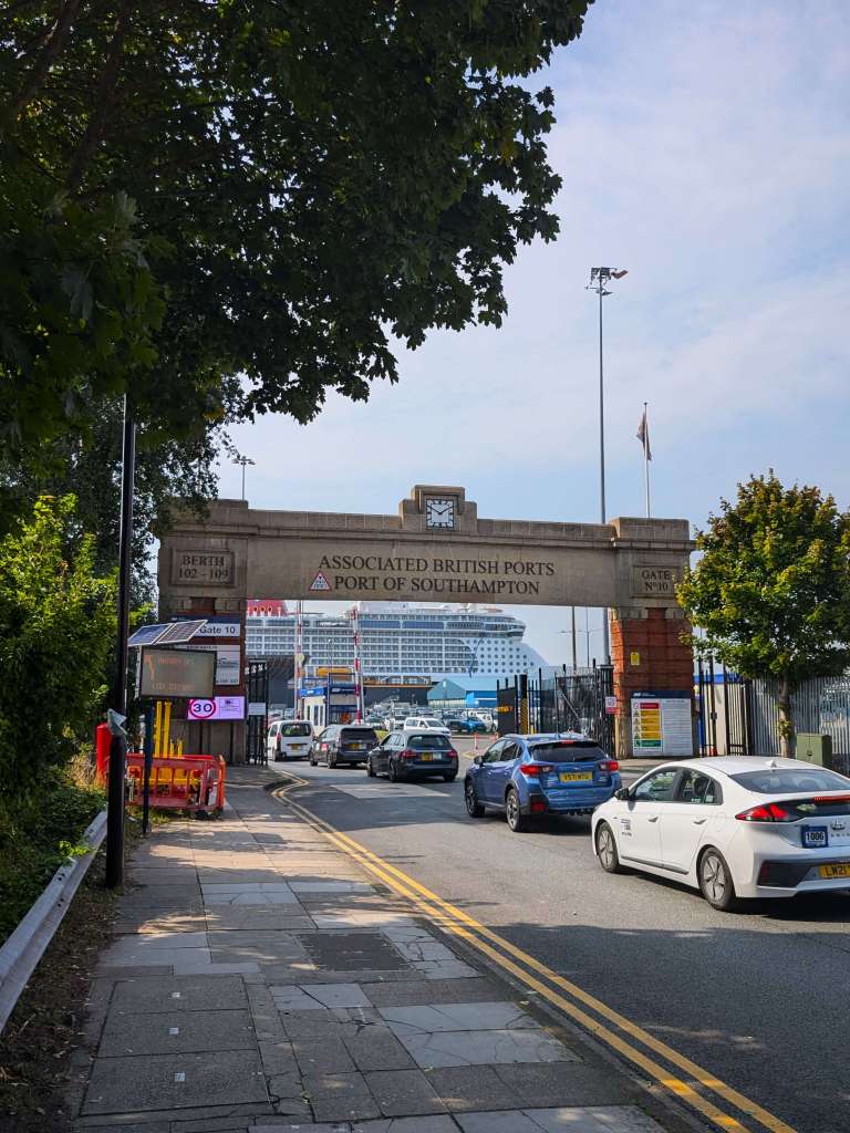 A line of cars driving under concrete archway of Port of Southampton with a cruise 